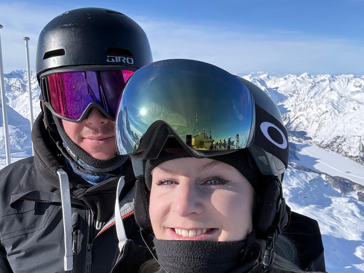Robin Heer und Melanie Meier, die Gründer von SnowRabbit, mit Helm und Skibrille auf einem Gipfel im Engadin, dahinter verschneite Berge unter blauem Himmel
